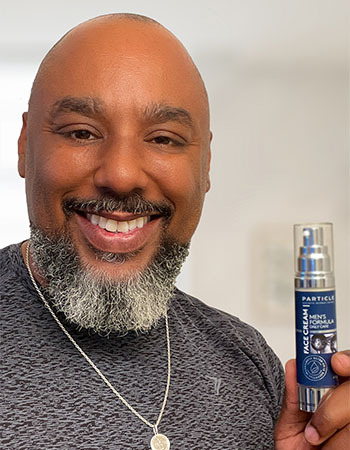 A smiling man holds a Particle Face Cream bottle.