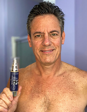 Man holding Particle skincare product bottle, smiling, standing in bathroom.