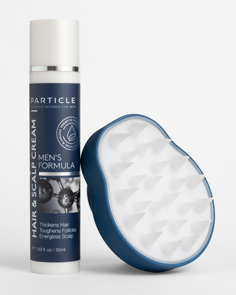 A bottle of Particle Hair & Scalp Cream Men's Formula and a blue scalp massager.