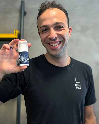 A smiling man holding a Particle Scar Gel bottle.