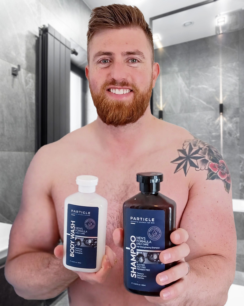 Man holding Particle Body Wash and Shampoo bottles in modern bathroom.