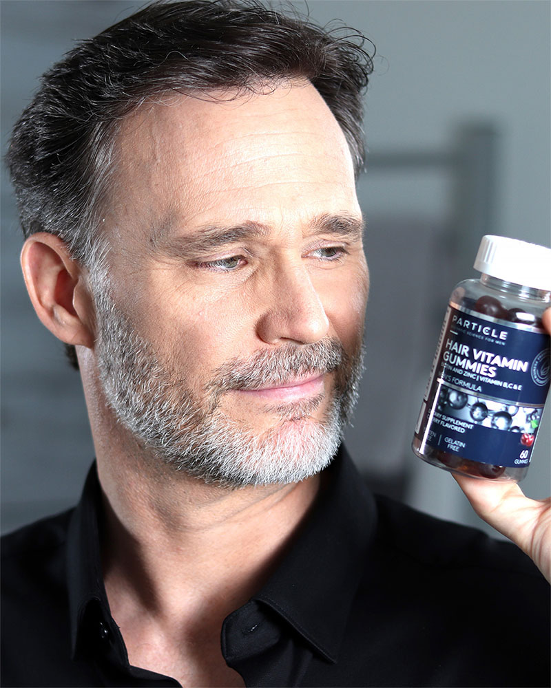 Man holding a bottle of Particle Hair Vitamin Gummies with white cap.