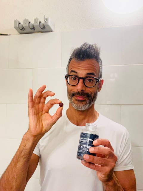 Man holds vitamin gummy and a bottle of Particle Hair Vitamin Gummies.