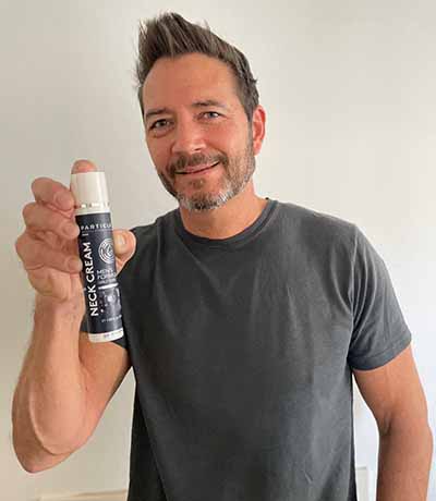 Man in gray t-shirt, holding Particle Neck Cream.