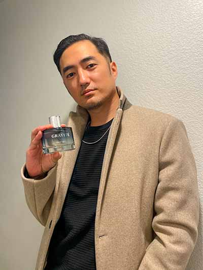 Man holding perfume light blue bottle with metallic cap labeled Gravité Particle.