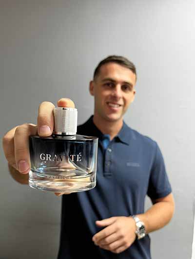 A man holds a bottle of Gravité Particle perfume in front of him.