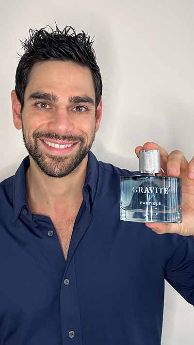 Man smiling holding Gravité Particle perfume blue bottle.