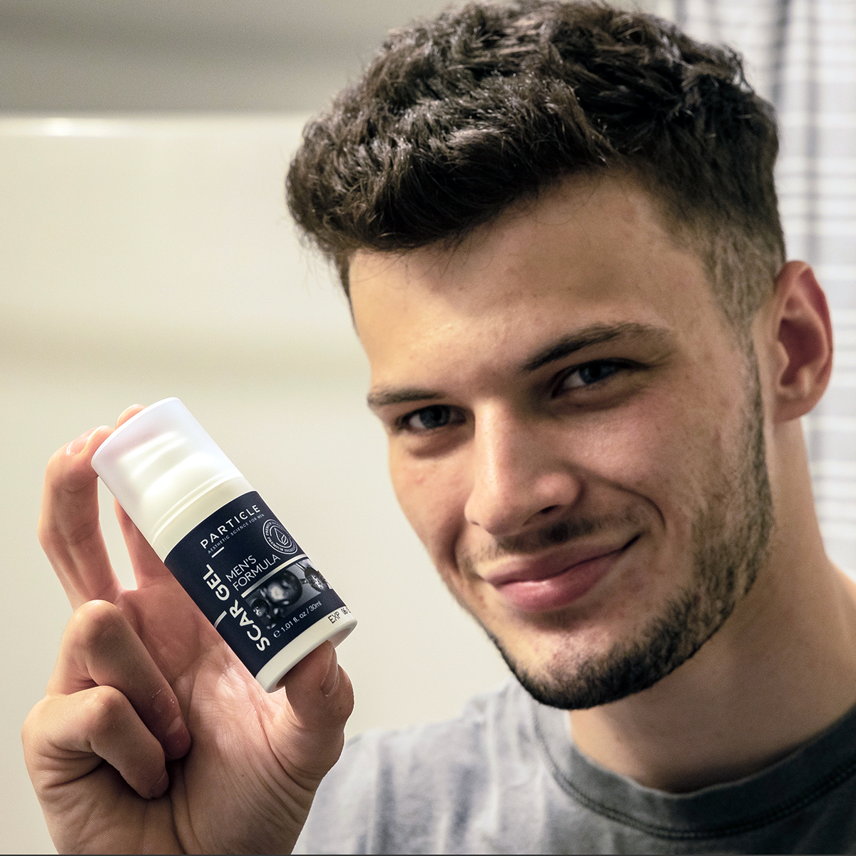 Young man holding Particle Scar Gel Men's Formula bottle.