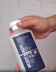 Hand holding bottle labeled Particle Body Wash in shower